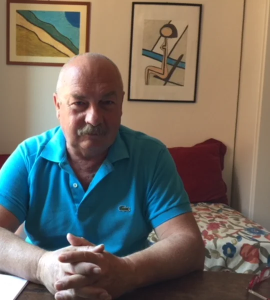 Stefano Zan, seduto a un tavolo con le mani giunte
